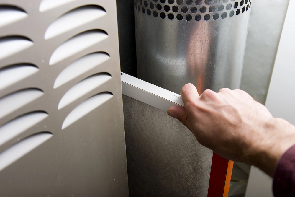 A hand is removing a dirty air filter from a residential furnace for replacement or maintenance.